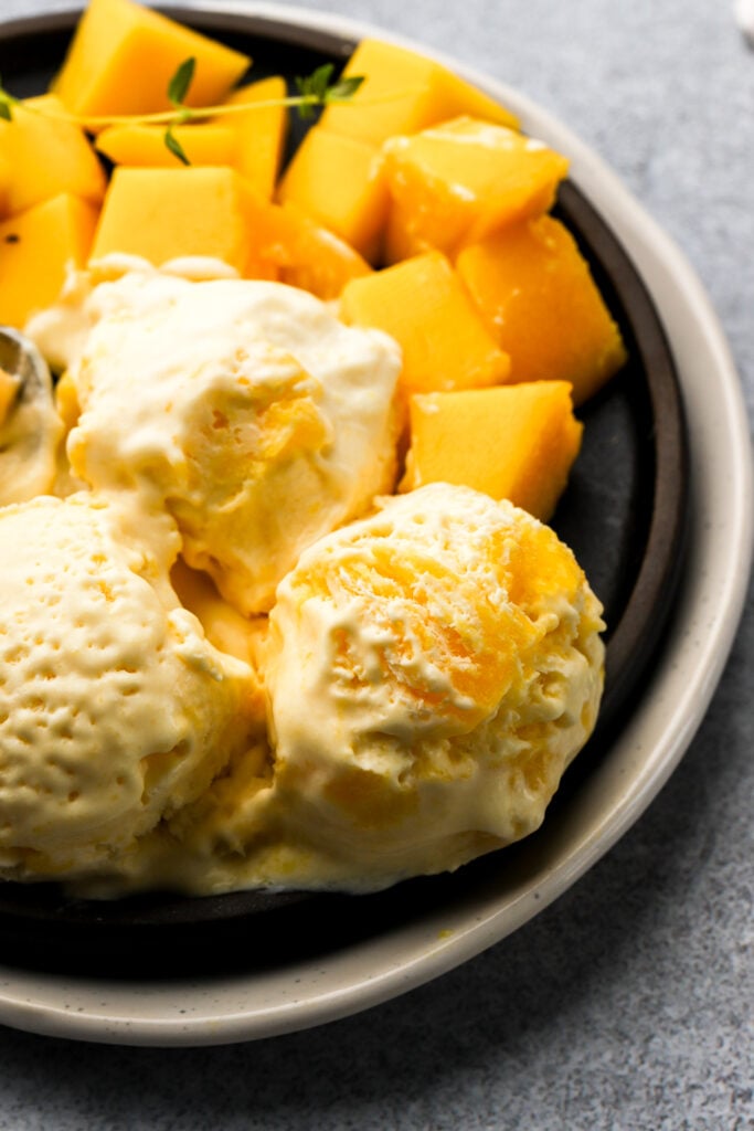 scoops of mango ice cream on a plate with fresh mangos