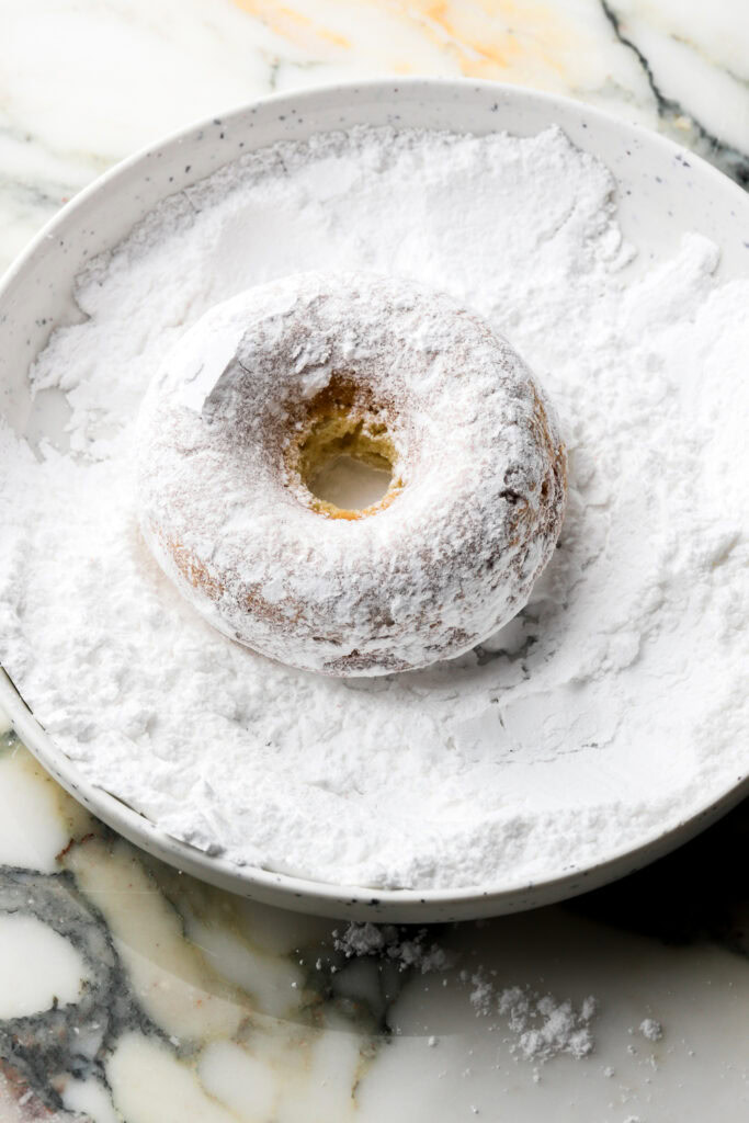 large donut tossed into powdered sugar
